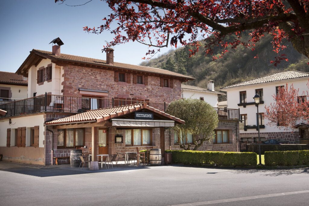 Imagen del Restaurante. se ve una gran casa de piedra rojiza de pueblo, con una amplia entrada