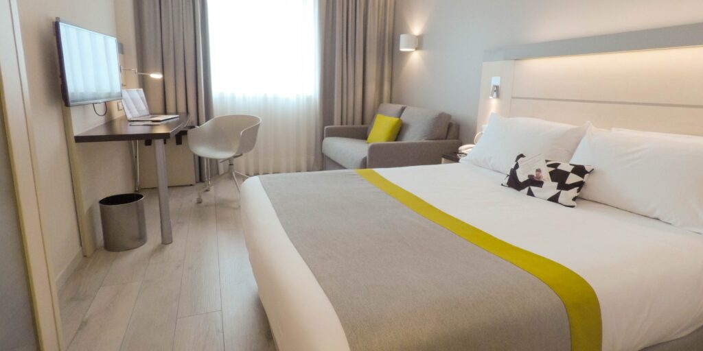 Habitaciñon con cama doble, decorada en tonos blancos, grises y mostazas