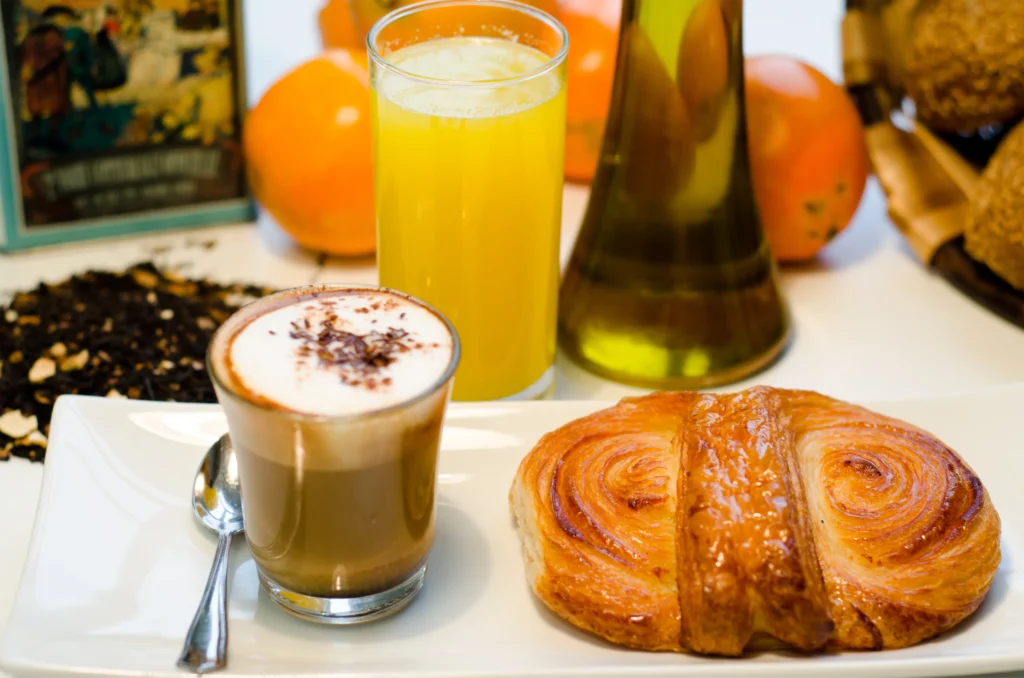 Desayuno con un café, zumo y un bollo, Se ven Naranjas y aceite de fondo