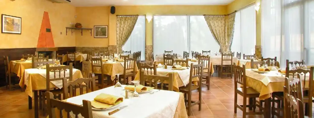interior del restaurante. Sillas de madera, con mesas cubiertas con mantel amarillo y blanco y la pared amarilla.