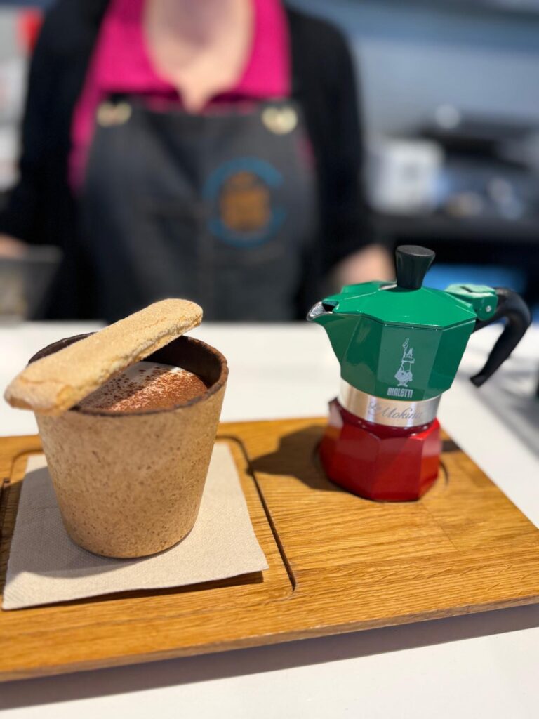 Vaso comestible con bebida de especialiad y una cafetera francesa a su lado derecho