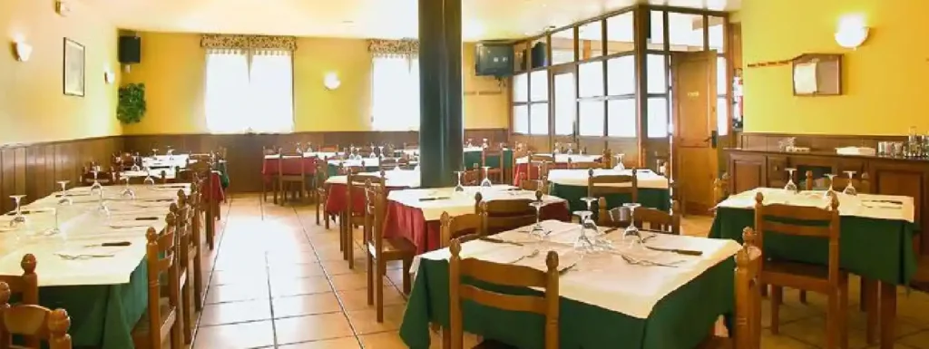 interior del restaurante, con mesas y sillas de madera, manteles rojos y verdes y la pared amarilla