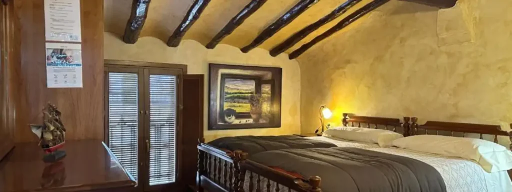 habitación con dos camas grandes y techo abuardillado, pared pintada a aguas en tonos amarillos y moviliario de madera oscura