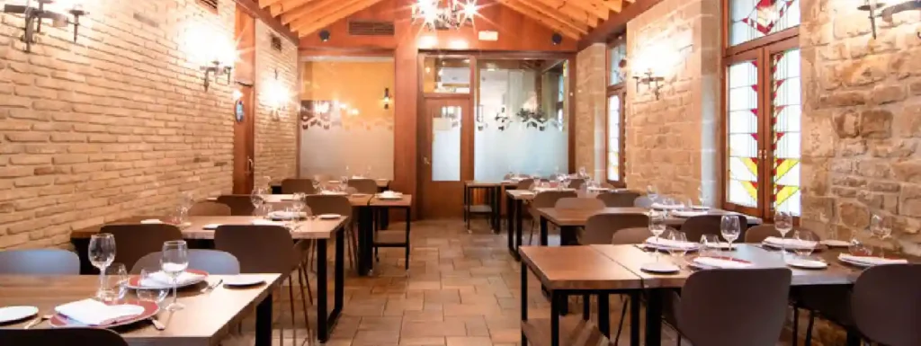 interior del restaurante con mesas de madera y pared de piedra