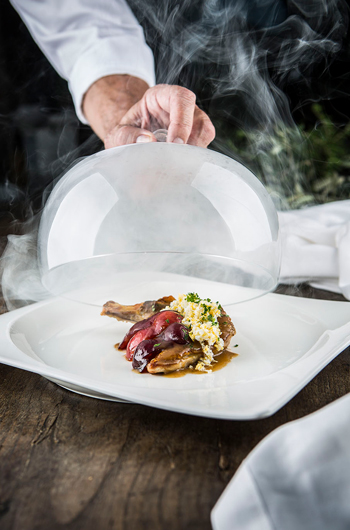 Plato del Restaurante Pago de Cirsus una mano levanta una campana que contenía el plato