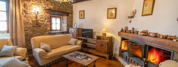 Salon con sofas al rededor de una mesa cuadrada central, con una chimenea de leña n la esquina superior derecha.