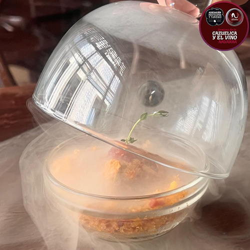 Inspirada en los pastores de la montaña navarra que aprovechaban el pan duro y guisaban el cordero al calor de la lumbre. Se presenta con una chispa de gel de piquillos, toque ahumado de sarmiento, homenajeando a las viñas de Navarra, y un final dulce.