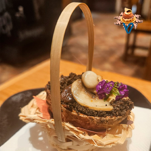 Crujiente de patata, relleno de espuma de hongo cubrimos con una tierra de trompeta de la muerte y terminamos poniéndole setas variadas y una flor, representando la tierra húmeda de donde nacen las setas.