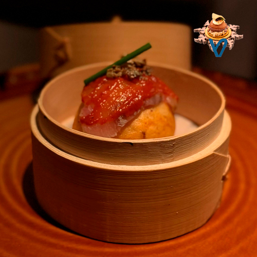 Pan bao de piquillos casero relleno de corvina marinada, un bocado delicado donde la suavidad y el ligero dulzor del pan envuelven la frescura y la textura sedosa del pescado. Equilibrado, aromático y lleno de matices.