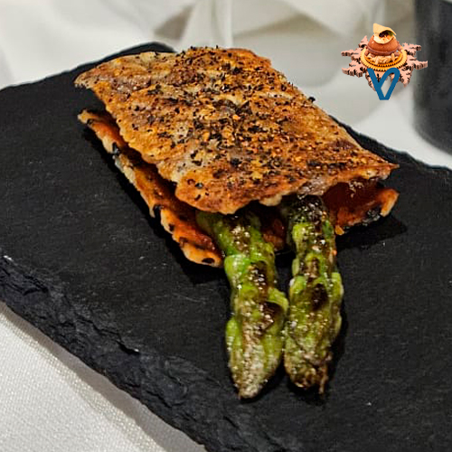 Dos puntas de espárrago trigueros cubierta por dos crujientes una de manitas de cerdo deshuesada y otra de una galleta casera de arroz y sésamo con una salsa de sriracha casera de piquillo ralladura de lima y un polvo de las pieles del piquillo.