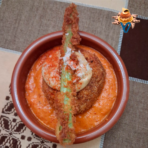 Una base de crema de pimientos del piquillo, emulsionados con aceite de oliva/ pelota de chistorra navarra envuelta en en costra de panko con pimentón de la vera/ crujiente de borraja/coronado con un alioli de ajo negro todo ello terminado con unas escamas de sal maldón y un toque de polvo de chile coreano.