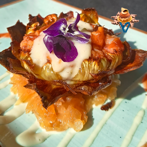 Alcachofa de Navarra confitada a baja temperatura y frita en su finalización, se rellena de manitas de cerdo deshuesada y callos de ternera cocinados de forma que nos enseñaron nuestras ABUELAS, cubierta por una parmentier de patatas y espárragos…regada con su salsa y decorada con pétalos.