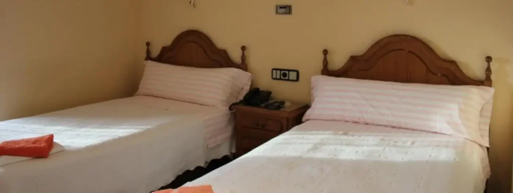habitación doble con dos camas individuales y cabecero de madera, sabanas a rayas