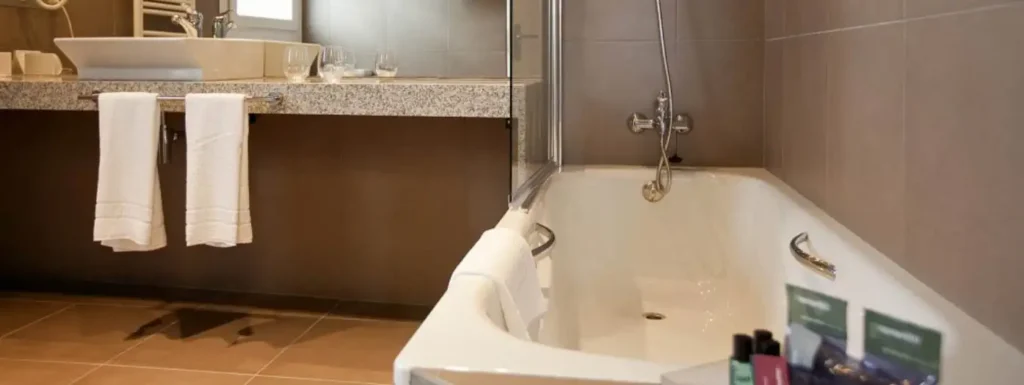 aseo completo con la bañera a la derecha y los articulos de aseo. En el fondo, el lavabo con dos toallas