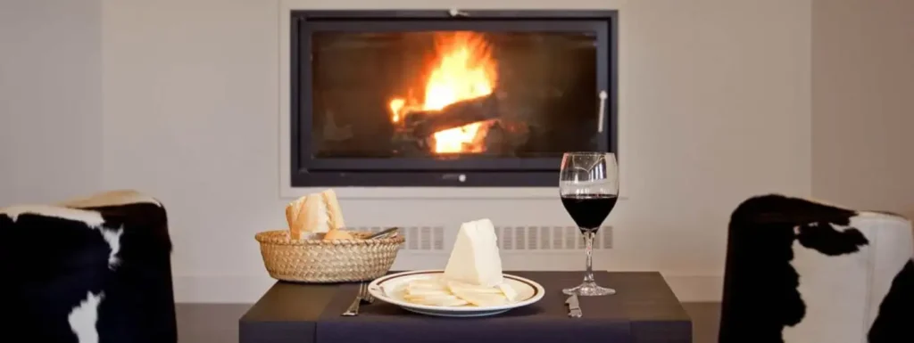 pared blanca con una chimenea incustrada en ella, en primer plano una mesa con vino, queso y pan