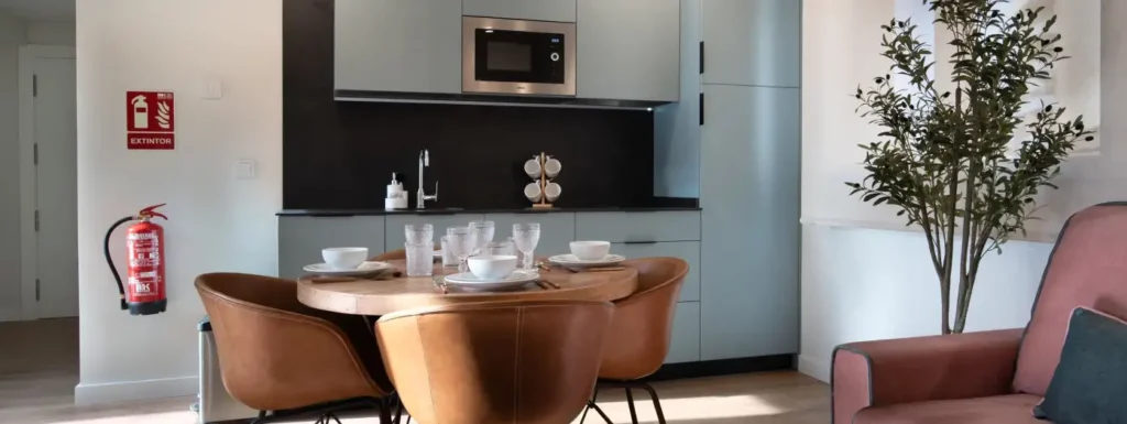 Cocina empotrada, azul clara con detalles en negro. Delante una mesa circular con cuatro sillas de piel marrones