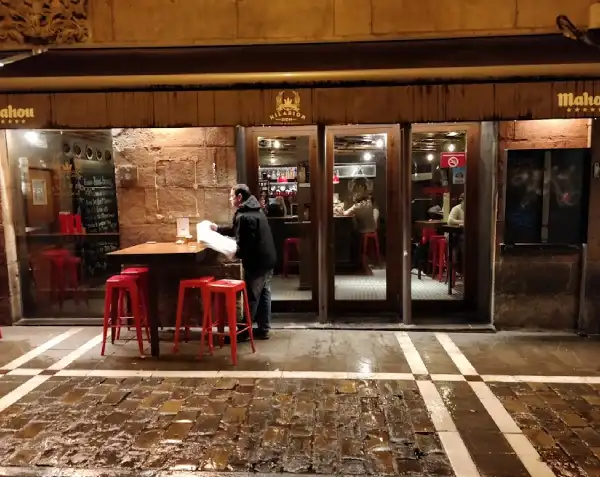 Entrada del Bar Don Hilarión, Puertas de cristal, con una mesa alta con sillas en un lateral
