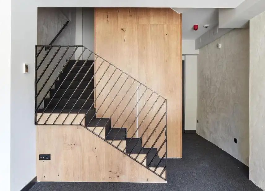 Escaleras en madera clara y detalles en negro con paredes de cemento