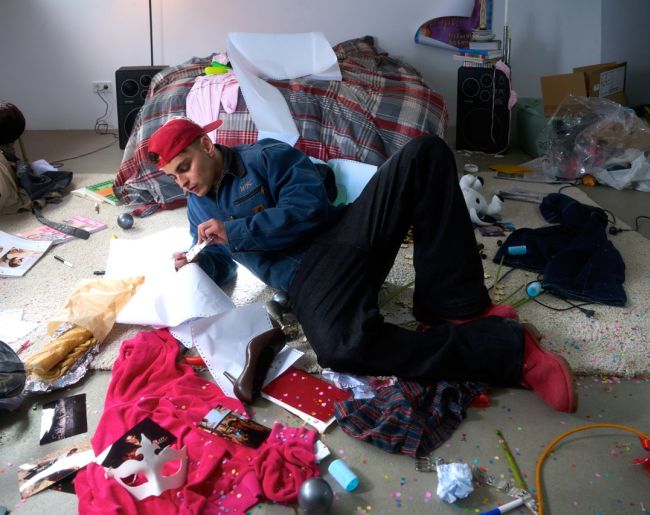 funzo tumbado en el suelo su una habitación totalmente desordenada, sucia y todas las cosas por el suelo.