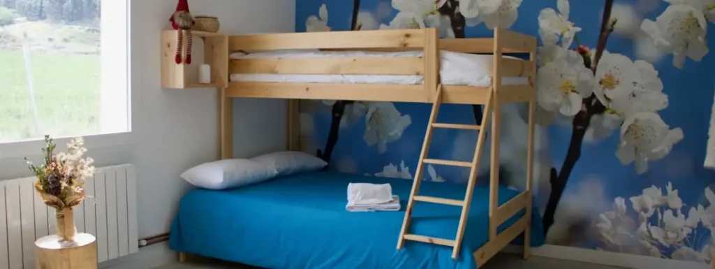 litera con cama de matrimonio abajo y cama individual arriba. Pared con imagen de flor de almendro
