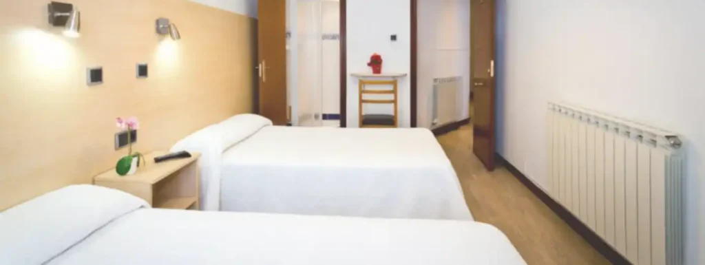 habitación con dos camas y en la parez del fondo dos puertas, a la izquierda el aseo a la derecha la entrada de la habitación