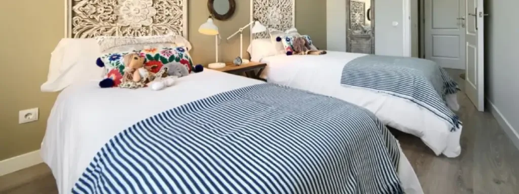 habitación con dos camas independientes, con sabanas a rayas y muñecos infantiles sobre las colchas