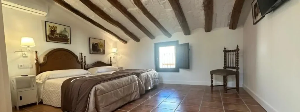 amplia habitación doble, con dos camas con cabecero de madera, colores claros con vigas de madera oscura en el techo