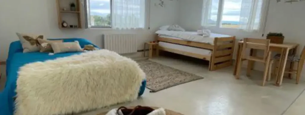 habitación con cama amplia y manta de borrego encima, sabanas azules y una cama infantil en el fondo