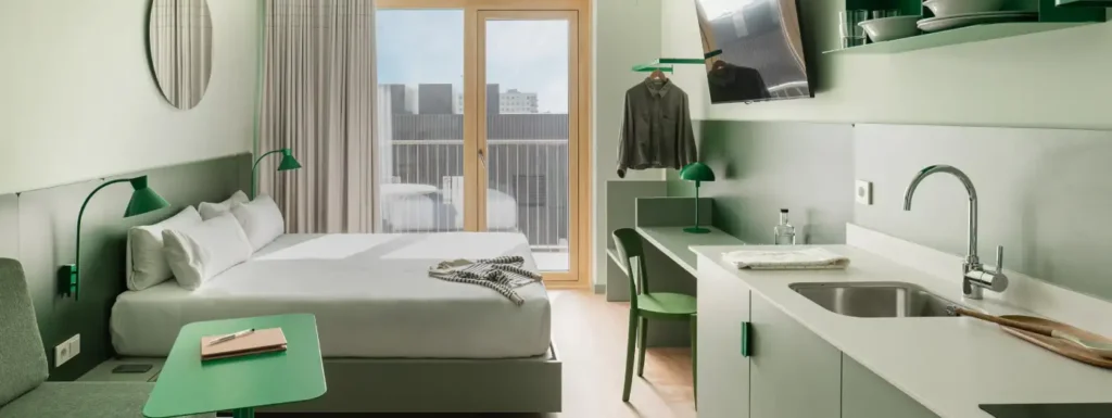 apartamento en tonos verdes menta, doble cama indvidual, con cocina a la derecha y ventanal con terraza al fondo