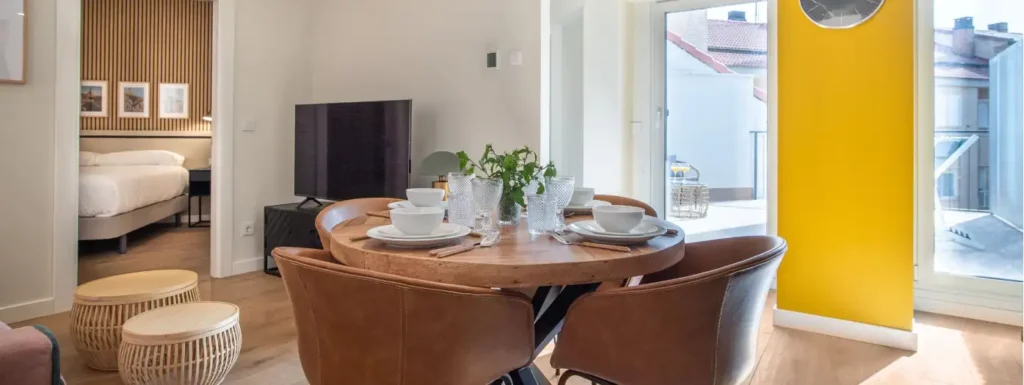 mesa circular con sillones de piel. Al fondo a la derecha la salida a la terraza y a la izquierda la entrada a la habitación.