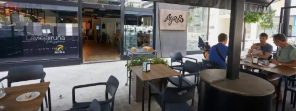 Terraza y entrada al establecimiento. Mesas y sillas de terraza y una entrada acristalada