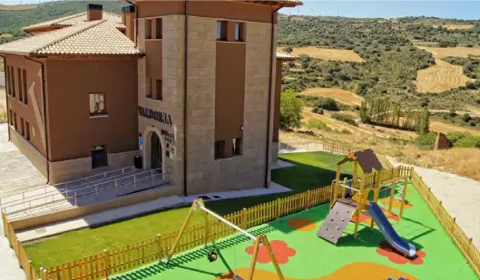 vista de pajaro del hotel valdorba, se ve el edificio al fondo de piedra rustica rojiza y un parque infantil en la parte inferior