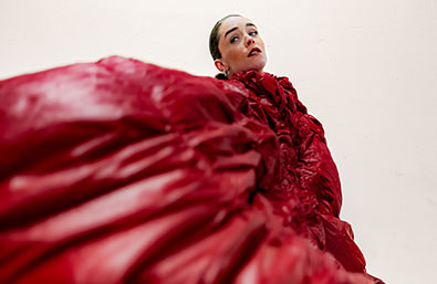 ángulo bajo sobre fondo claro. La imagen destaca el dinamismo del vestuario y la expresión intensa de la artista.