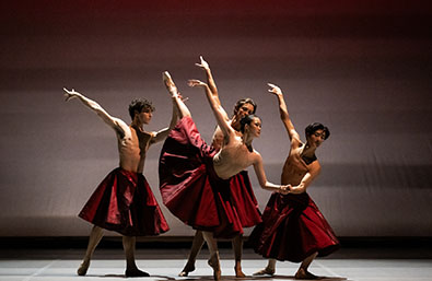 Cuatro bailarines interpretan una coreografía sobre un escenario, con vestuario en tonos burdeos y posturas de danza clásica contemporánea.