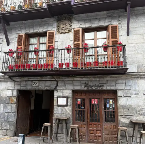 Fachada de piedra de casa de pueblo, con porton de madera y balcon con flores en la parte superior