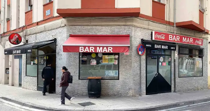 Bar en esquina con toldos rojos y amplias cristaleras