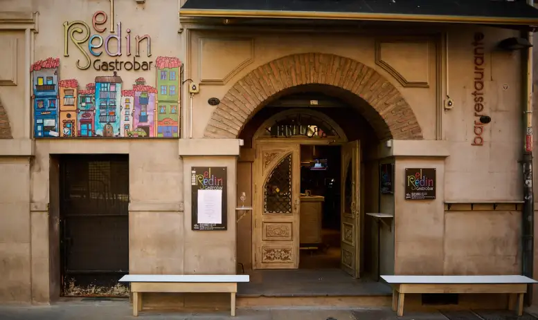 entrada con arco de piedra, con dos bancos en los laterales y una imagen colorida de los edificios de pamplona con estilo dibujo