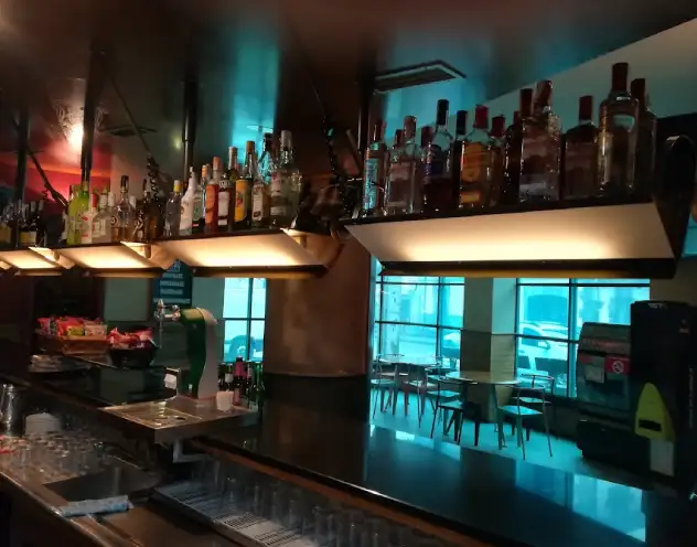 Imagen desde el interior de la barra, en la parte superior el botellero en la parte inferior las neveras, al fondo las mesas del establecimiento
