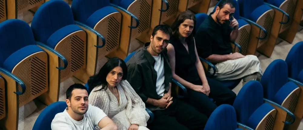 integrantes del grupo Nogen estsán sentados en un teatro mirando hacia arriba, haci a la cámara de fotos.