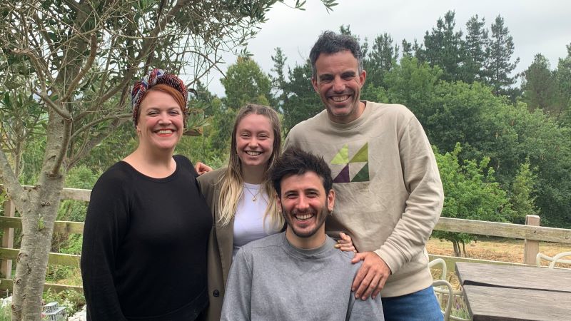 Cuatro personas posan sonrientes en grupo al aire libre, en un entorno natural con árboles y vegetación al fondo.