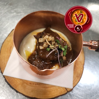 Carrilleras guisadas lentamente con cacao latam y aji panca, cremoso de papa asada y perlitas de zanahoria y calabacín salteadas al panca